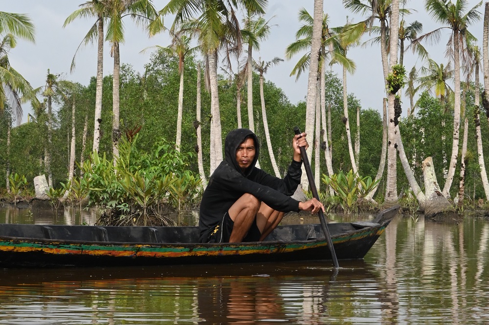 Seorang nelayan mendayung perahu sampan di bekas kebun kelapa yang terendam air laut di Parit 18 Kelurahan Sapat (Wahyudin Opu/Blue Forests)